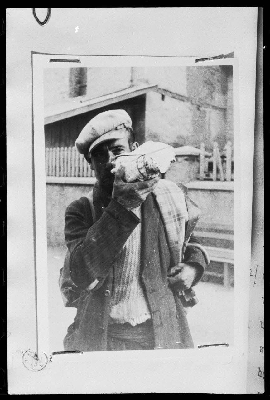 Jeannine Auboyer photographie Monsieur Clément dit "Barberousse", le vacher d'Aiguilles, parcourt le village en tous sens en sonnant la "conque marine", puis revient sur la place pour déposer sa conque. Les paysans conduisent leurs vaches et les confient au vacher. Les 68 vaches sont réunies Provence-Alpes-Côte d'Azur, France 1938/8/1 Ph.1975.103.1 Photo