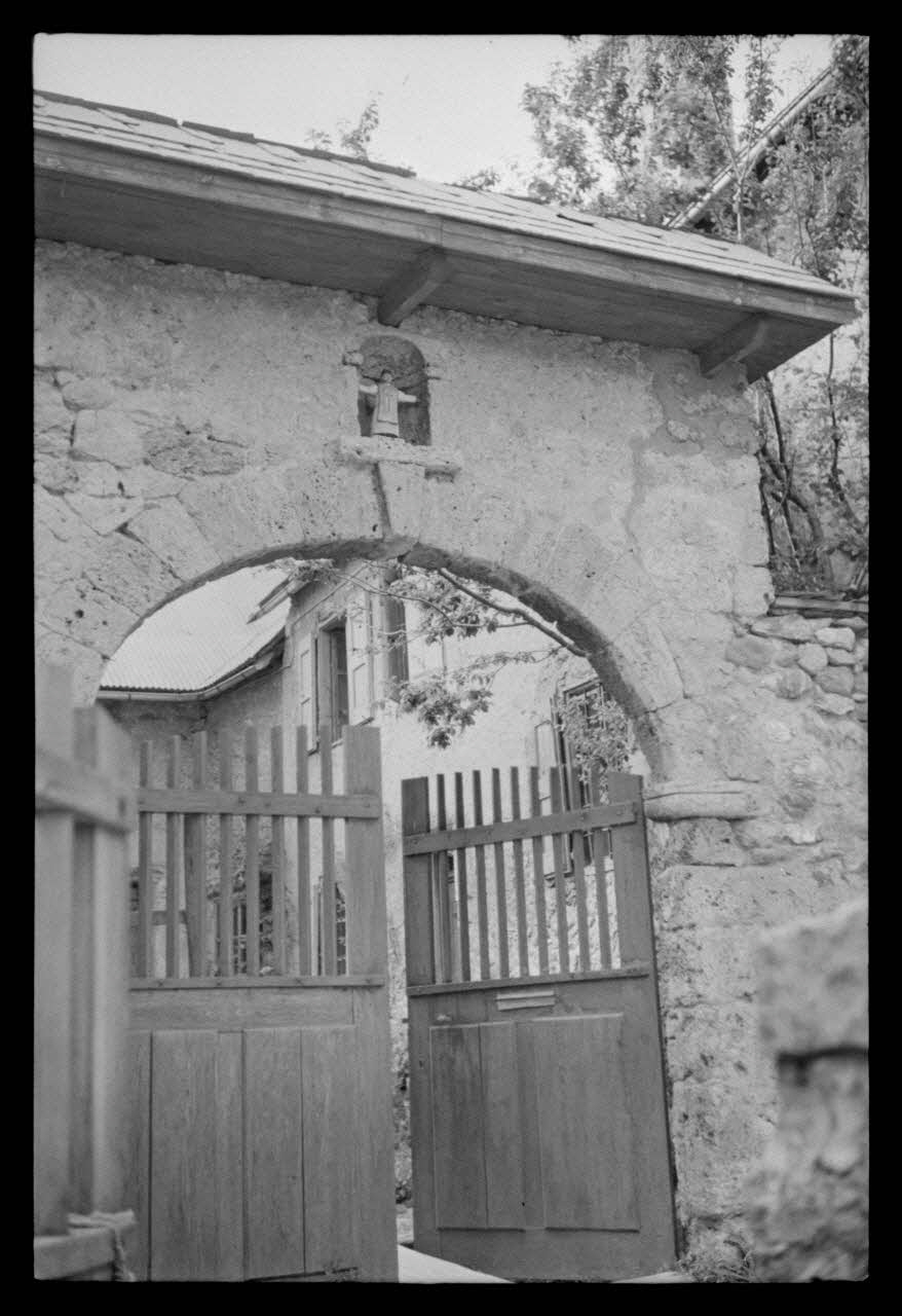 A. Jomelli ; B. Jomelli photographie Entrée du presbytère avec portail et niche abritant une statue polychrome de saint Claude. Deux battants en bois plein et bois à clairevoie ferment la cour Provence-Alpes-Côte d'Azur, France 1966/7/21 Ph.1966.119.73 Photo