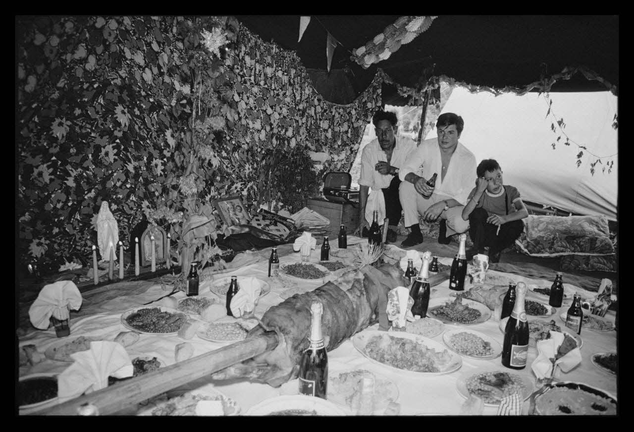 Philippe Lemaire De Marne photographie Roms, nomades "Kalderash". Fête traditionnelle "Prasmiko". Famille de "Papa" Gusman et Théodore Gusman, son frère dans un terrain loué à la sortie du village. Table de Théodore. Roms à table Midi-Pyrénées, France 1965/8/15 Ph.1966.68.69 Photo
