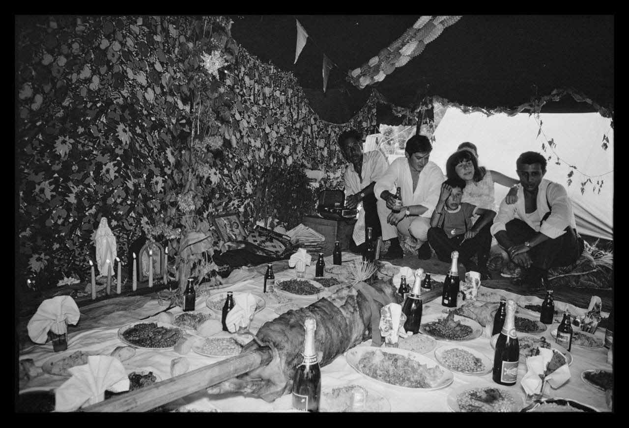 Philippe Lemaire De Marne photographie Roms, nomades "Kalderash". Fête traditionnelle "Prasmiko". Famille de "Papa" Gusman et Théodore Gusman, son frère dans un terrain loué à la sortie du village. Table de Théodore. Roms à table Midi-Pyrénées, France 1965/8/15 Ph.1966.68.70 Photo