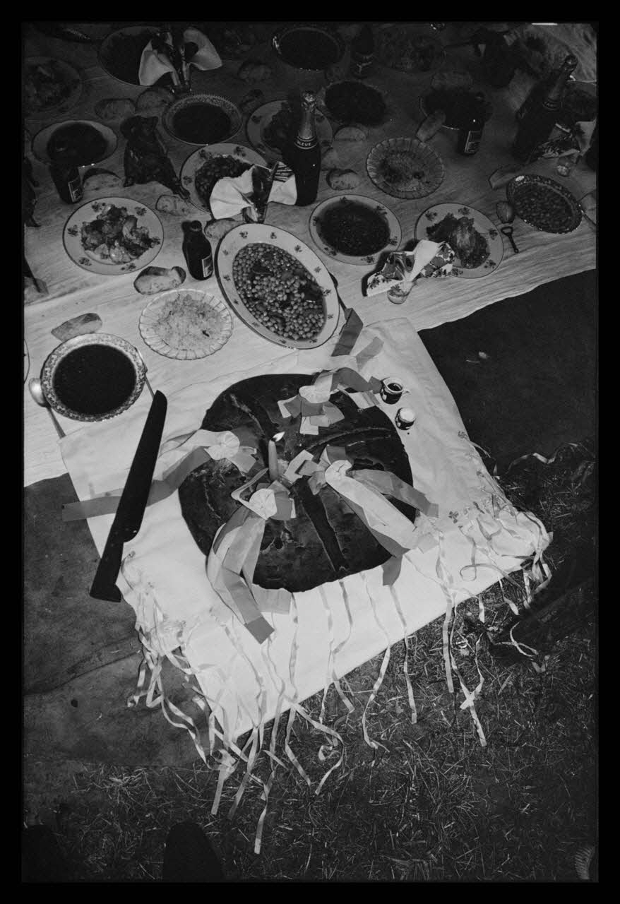 Philippe Lemaire De Marne photographie Roms, nomades "Kalderash". Fête traditionnelle "Prasmiko". Famille de "Papa" Gusman et Théodore Gusman, son frère dans un terrain loué à la sortie du village. Gâteau "Kolako" avec un couteau, une bougie allumée, un pot de vin et du sel Midi-Pyrénées, France 1965/8/15 Ph.1966.68.72 Photo