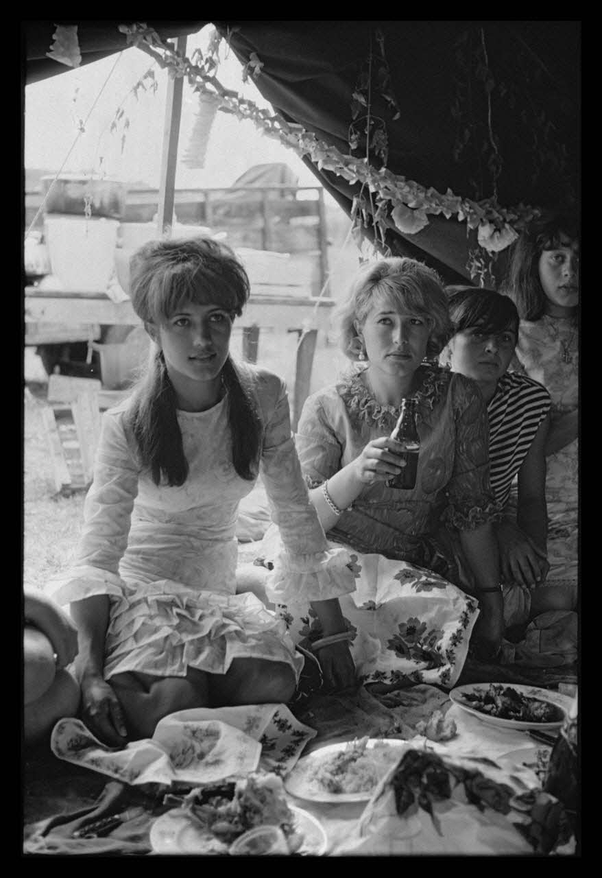 Philippe Lemaire De Marne photographie Roms, nomades "Kalderash". Fête traditionnelle "Prasmiko". Famille de "Papa" Gusman et Théodore Gusman, son frère dans un terrain loué à la sortie du village. Jeunes filles de Papa à table Midi-Pyrénées, France 1965/8/15 Ph.1966.68.83 Photo