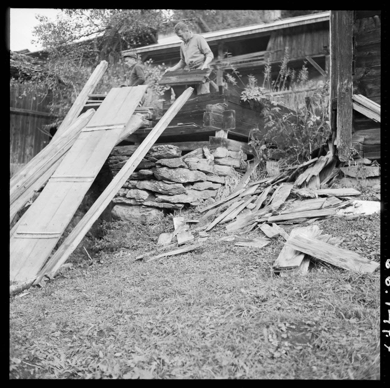 Jacques Pasquet photographie Grenier savoyard simple. Opération de démontage. Dans les mains du charpentier, un des madriers de façade. On remarque l'assemblage d'angle des madriers inférieurs, un potelet et deux sablières basses. Au premier plan, des madriers, le panneau de façade du coffre à grain et ancelles Rhône-Alpes, France 1966/11/9 Ph.1966.147.7 Photo Mucem /Pasquet, Jacques