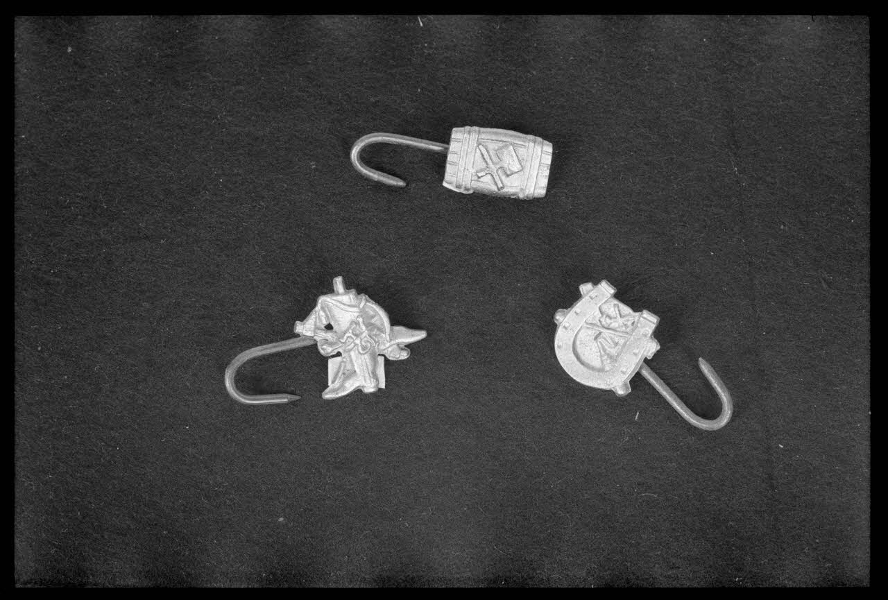 Alain Guey photographie Crochet de tablier de maréchal-ferrant fixés dans une plaque découpée représentant un cheval. Crochet de tablier de tonnelier fixés dans une plaque découpée représentant un tonneau. Crochet de tablier de bottier fixés dans une plaque découpée représentant des bottes Ile-de-France, France 1974 Ph.1974.63.64 Photo