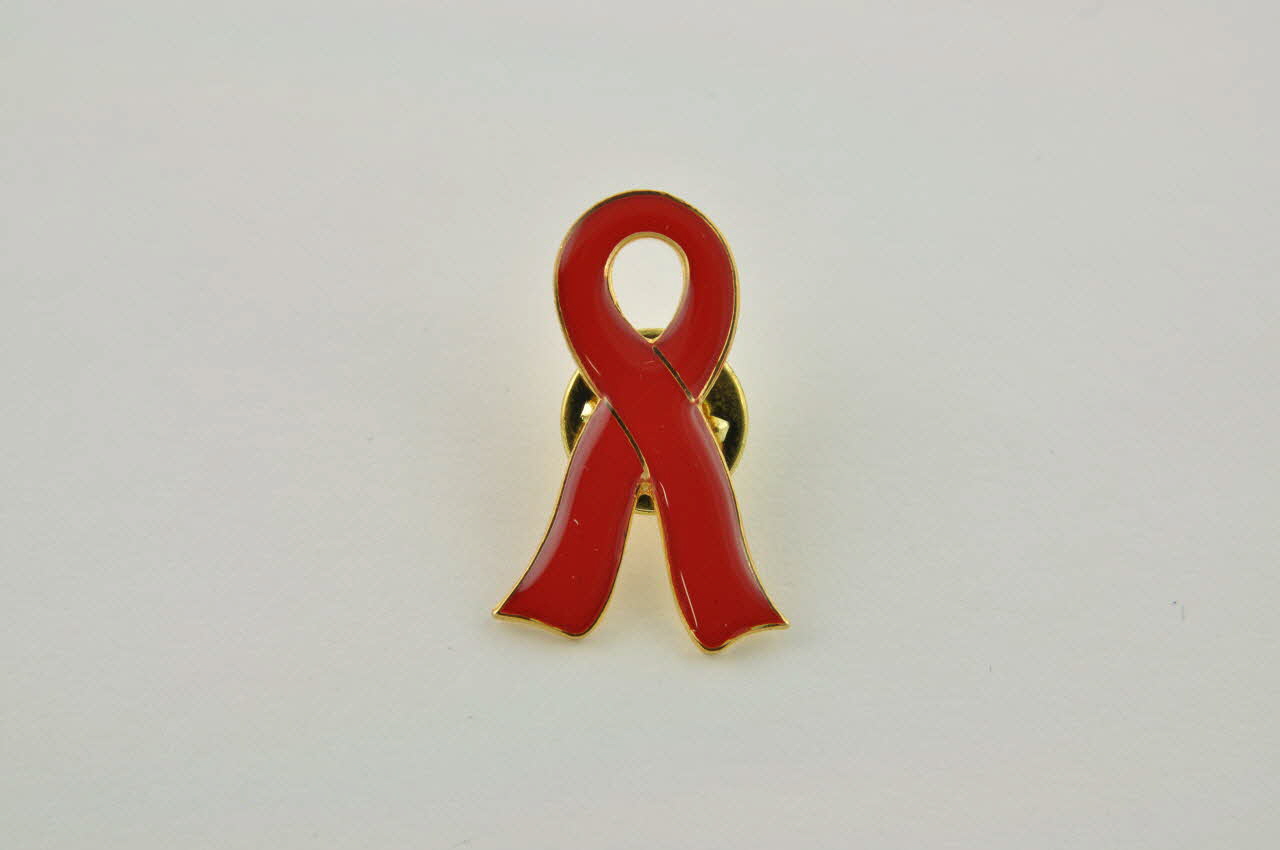 Pin's ruban rouge Pin's ruban rouge encerclé de doré, commentaire en arabe et en anglais 2005.119.48.1-3 Photo Mucem