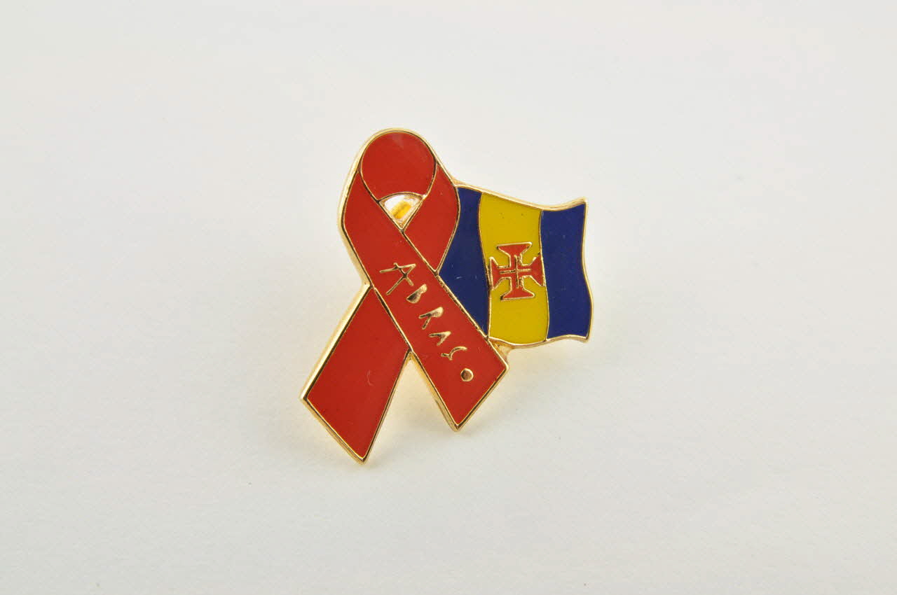 Pin's ruban rouge Pin's   ruban rouge entourant drapeau régional de Madère 2003.109.245.1-2 Photo Mucem