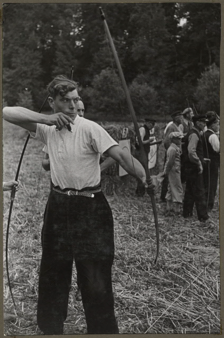 Madame Cartier photographie Dans le parc. Fête de Sylvie et des tireurs d'arc organisée par la Fédération folklorique d'Ile-de-France. La flèche vient de partir. L'arc est détendu Picardie, France 1938/6/19 Ph.1941.97.11 Photo