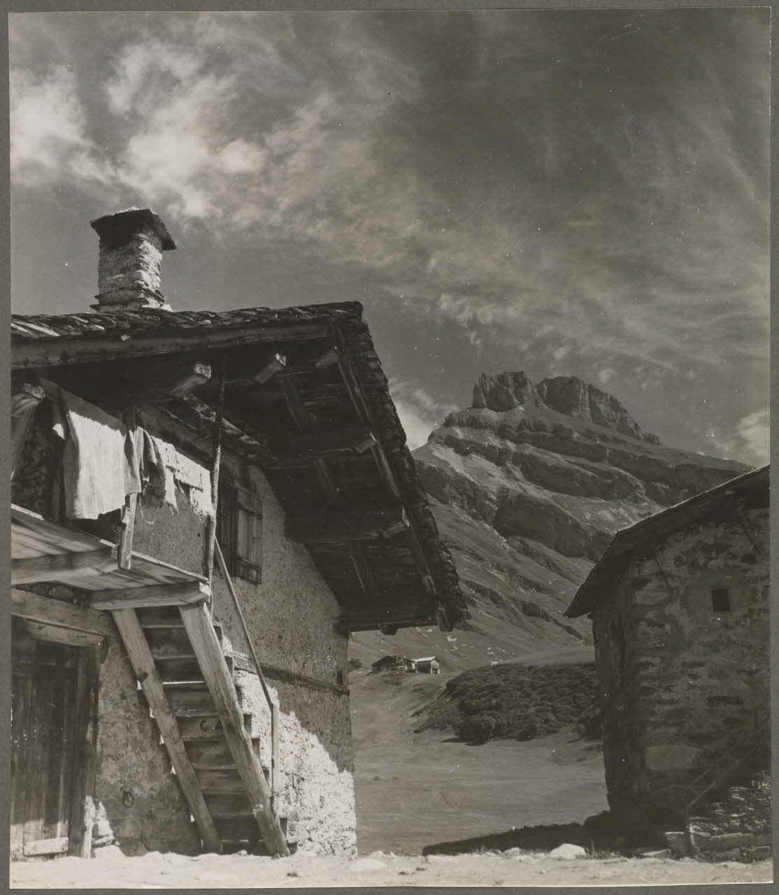 Bonis photographie Hameau de Roseland (temporaire). Chalet d'alpage, grosse maçonnerie enduite partiellement. Couverture en ancelles (écailles de bois fendues). Les rives du toit sont en lauzes (schiste). Au fond, le rocher du vent Rhône-Alpes, France 1945 Ph.1945.25.2 Photo