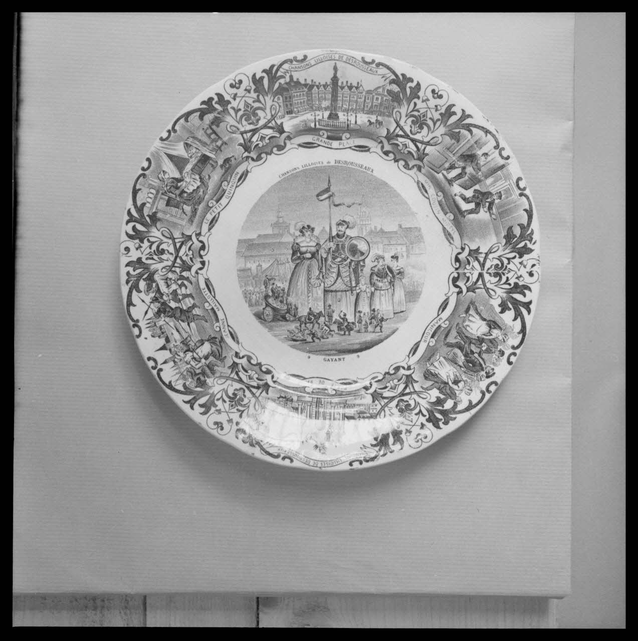 Bandy photographie Assiette en faïence noir et blanc. Au centre, inscription : "GAYANT". Sur le marli, des chansons lilloises de Desrousseaux Ile-de-France, France 1959/6/1 Ph.1959.102.2 Photo